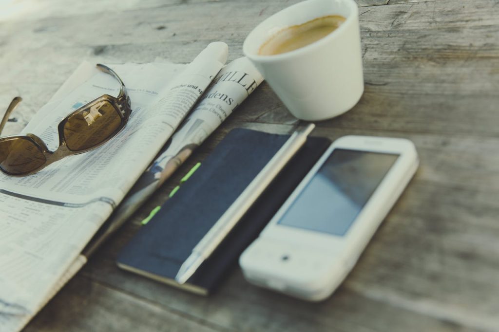 pexels-photo-218442 Relaxing scene featuring coffee, newspaper, sunglasses, notebook, and smartphone on a rustic wooden table.
